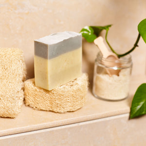Olive oil soap on a loofah sponge in the shower with a jar of scrub.