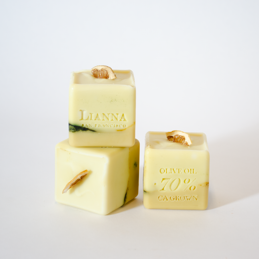 California olive oil soap in the shape of a cube with dehydrated lime wedges nestled on the top that are half white and half green/tan.